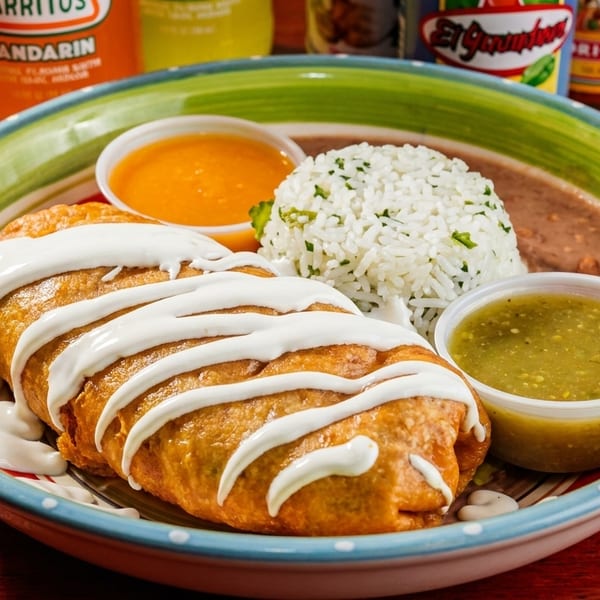 A deep-fried burrito drizzled with sour cream, served with rice, refried beans, and two dipping sauces.