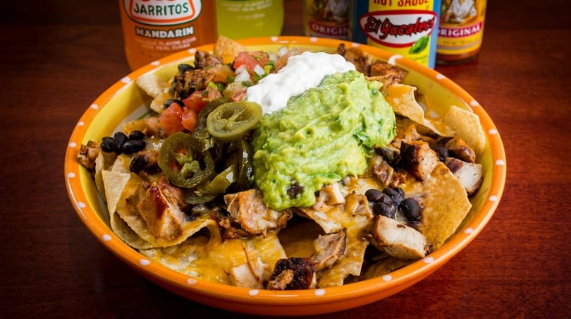 A bowl of chicken nachos with guacamole, sour cream, jalapeños, and black beans.