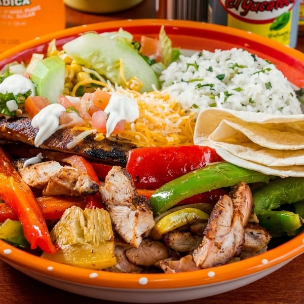 A colorful fajita bowl with grilled chicken, peppers, onions, rice, salad, cheese, and tortillas.